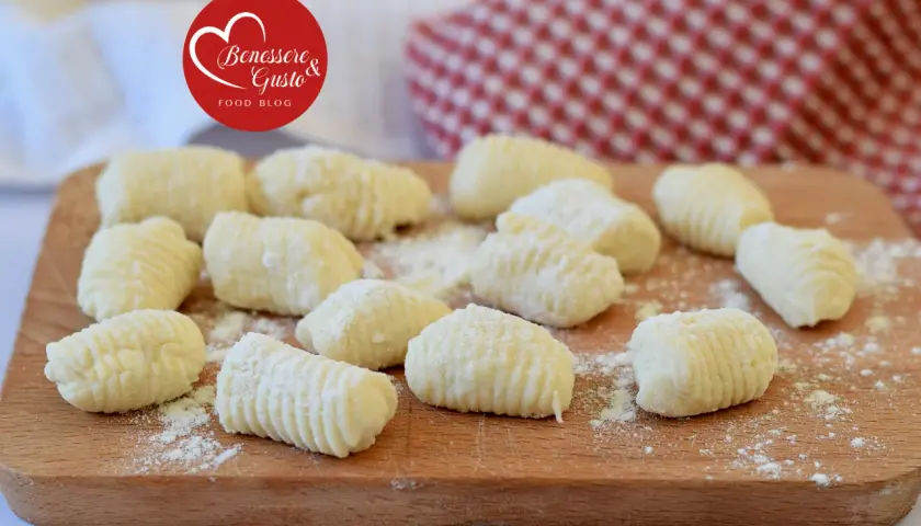 Gnocchi di ricotta freschi, pronti per essere cucinati, spolverati di farina su un tagliere di legno.