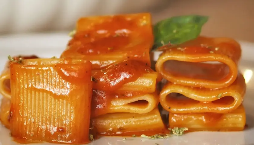 Un primo piatto invitante: paccheri conditi con un sugo rosso vivace, un classico della **pasta allo scarpariello**, guarnito con basilico fresco.