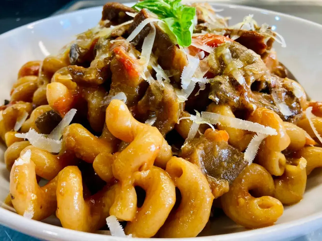 Un piatto invitante di pasta alla norma con melanzane, pomodoro e ricotta salata grattugiata, guarnito con basilico fresco.