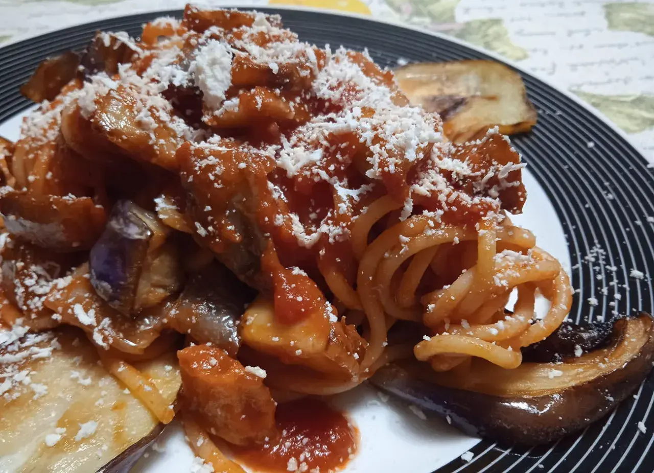 Un piatto invitante di pasta con melanzane, condita con sugo rosso e abbondante formaggio grattugiato.