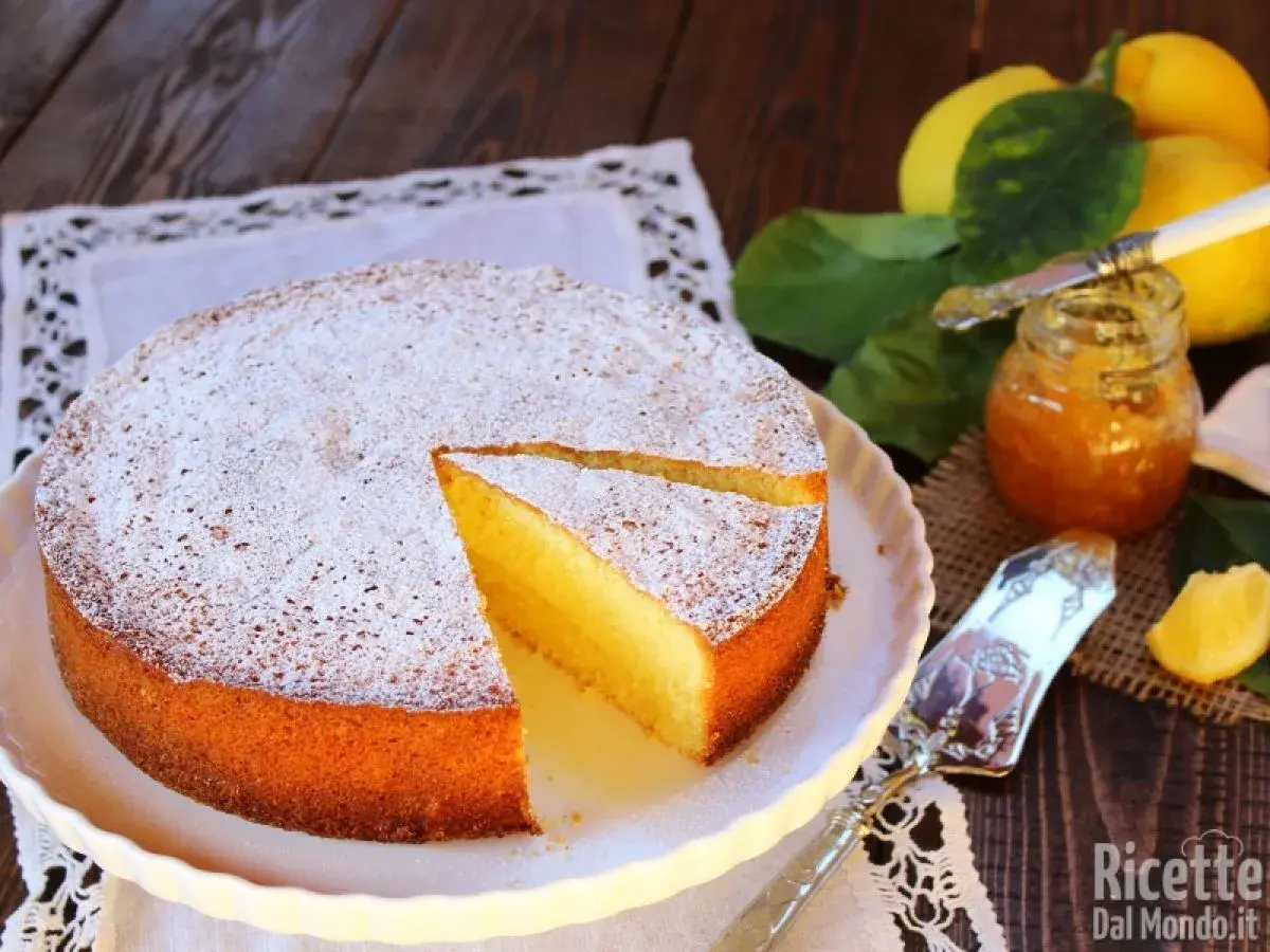 Una soffice torta al limone, spolverata di zucchero a velo, accanto a limoni freschi e marmellata.