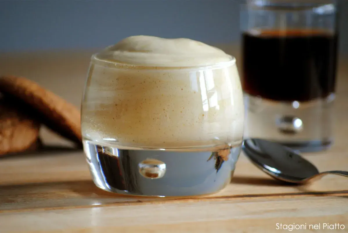 Delizioso zabaione ricetta in un bicchiere, con biscotti e caffè sullo sfondo.