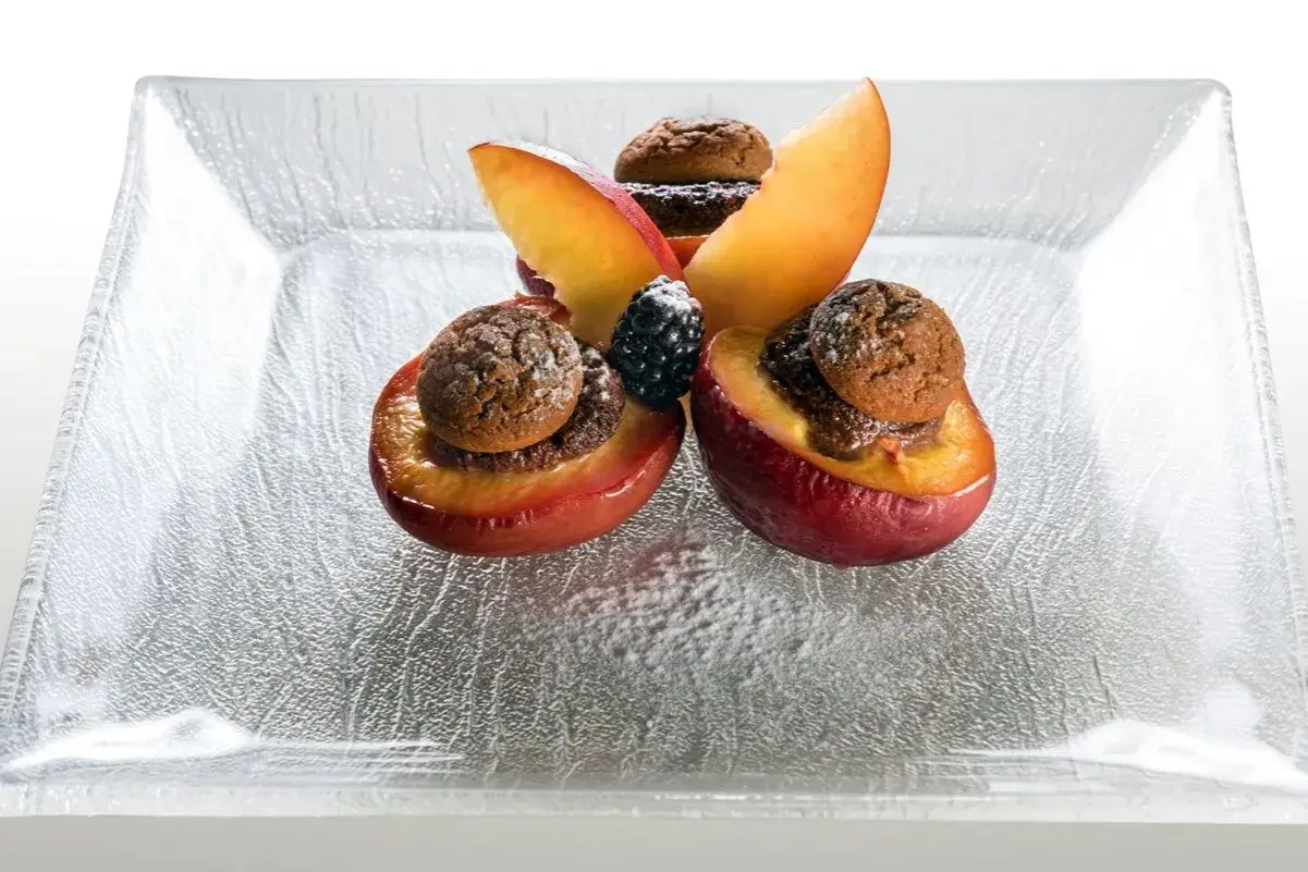 Deliziose pesche ripiene alla piemontese, guarnite con amaretti e frutti di bosco, su un piatto di vetro.
