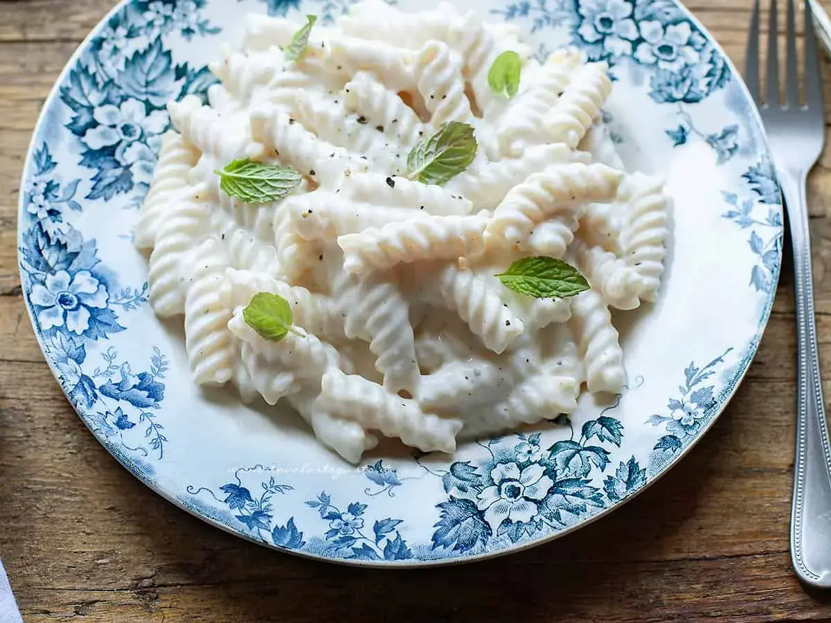 Fusilli cremosi con un sugo leggero alla ricotta, guarniti con foglie di menta fresca su un piatto decorato.