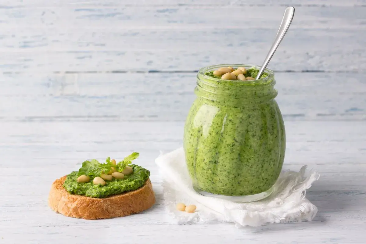 Pesto di rucola ricetta: un vasetto pieno di verde brillante e una bruschetta guarnita, pronti per essere gustati.