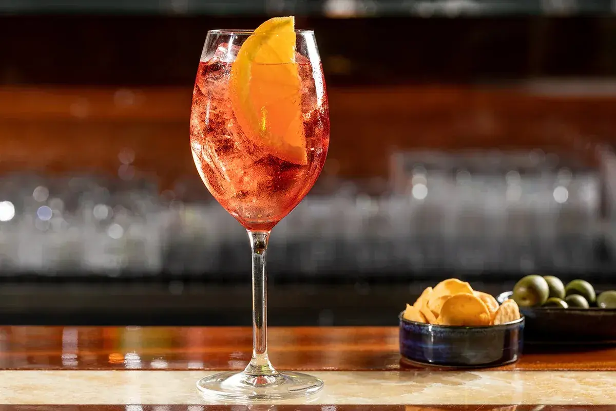 Un rinfrescante cocktail spritz, con una fetta d'arancia e ghiaccio, servito su un bancone di legno lucido.