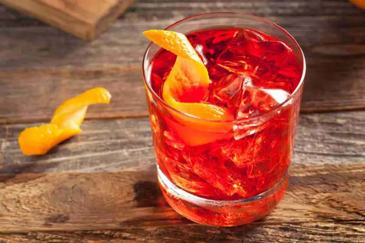 Un Negroni Sbagliato, con la sua vibrante gradazione di rosso, servito con ghiaccio e una scorza d'arancia su un tavolo di legno.