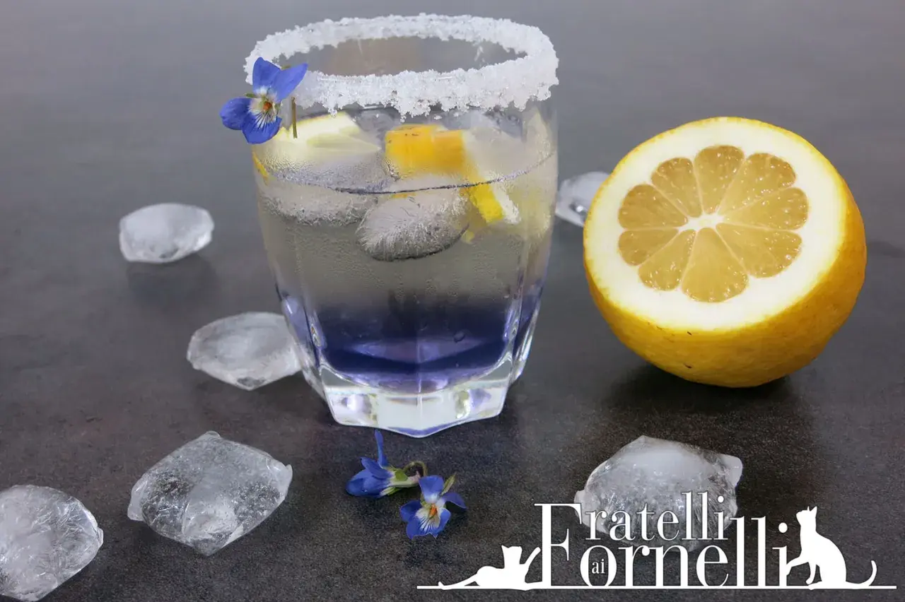 Rinfrescante liquore alla violetta spritz, guarnito con limone e fiori, circondato da cubetti di ghiaccio.