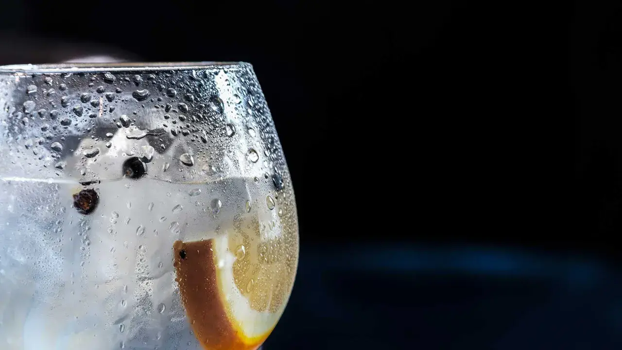 Bicchiere di gin tonic con ghiaccio, bacche di ginepro e fetta d'arancia. La **soda per spritz** rinfrescante crea goccioline sul vetro.