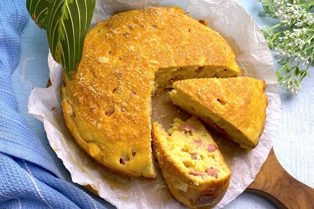 Torta salata prosciutto e formaggio dorata, con una fetta tagliata, su carta da forno.