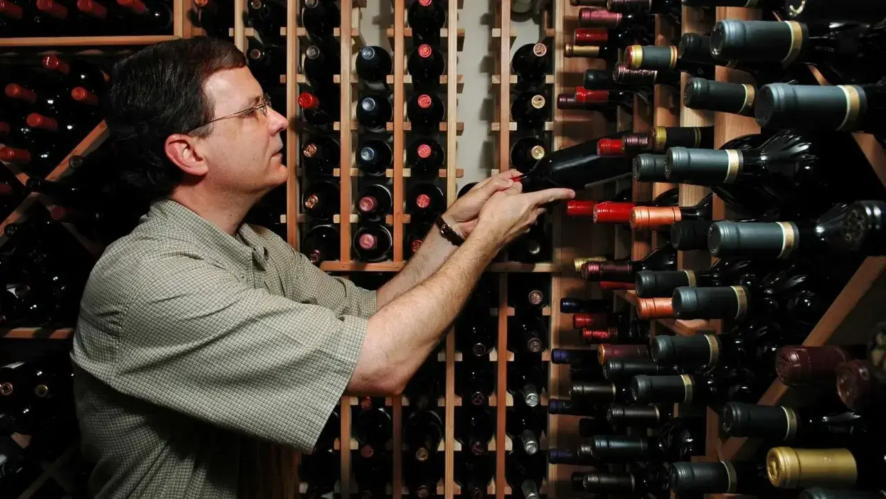 Un uomo sceglie tra una vasta cantina di cru vini, selezionando attentamente una bottiglia.