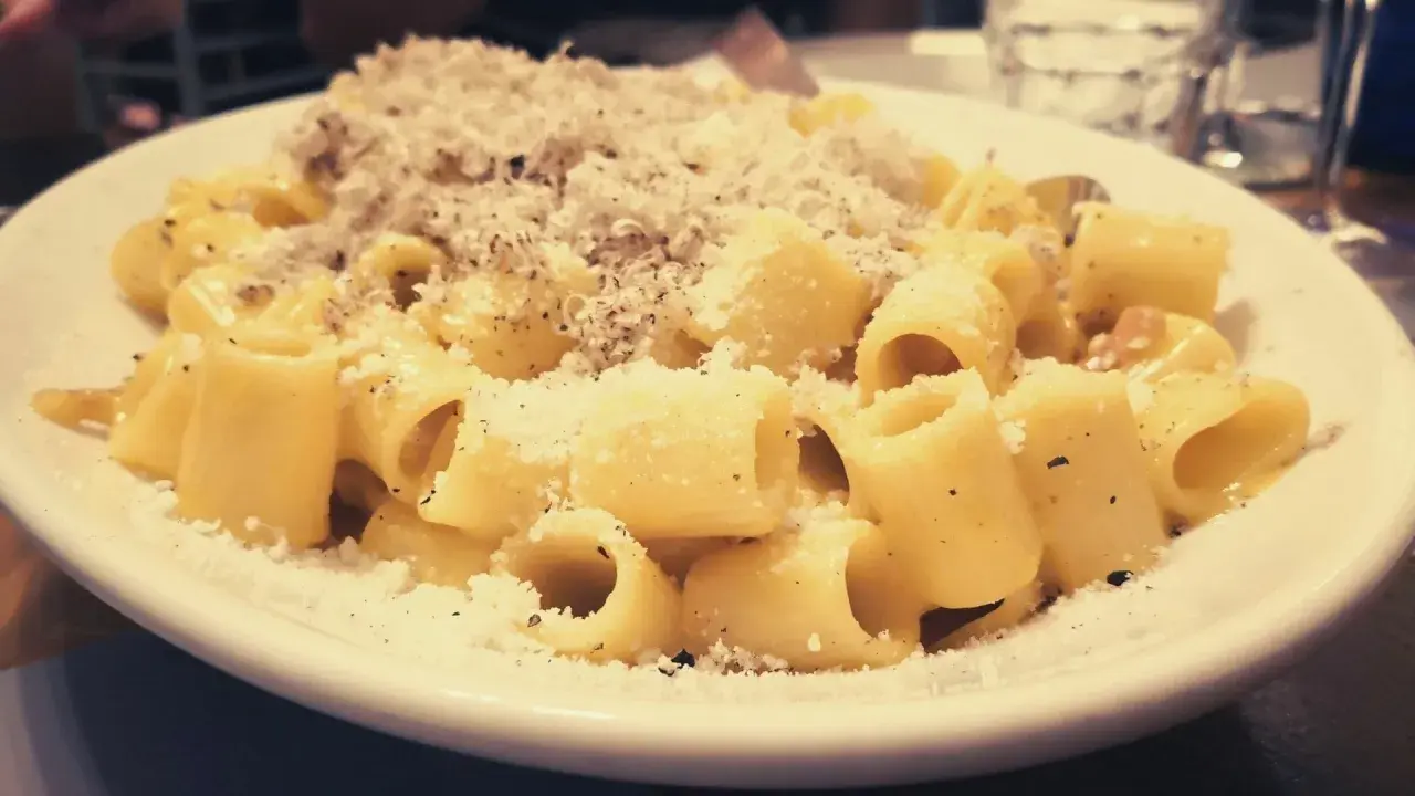 Piatto di carbonara fumante, cosparso di pecorino e pepe. Perfetta con un bicchiere di vino bianco o rosso.
