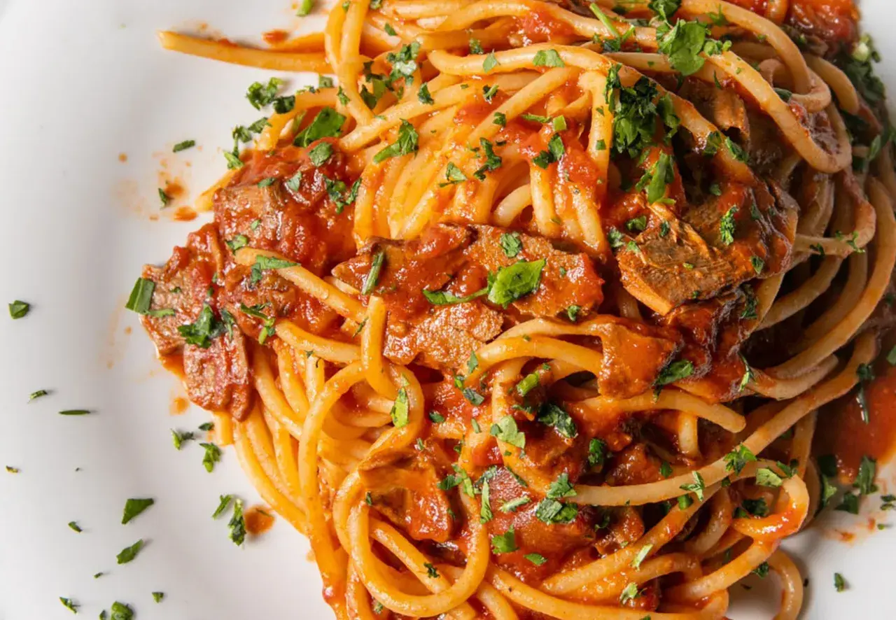 Spaghetti con tonno in scatola, un classico piatto veloce e saporito, condito con sugo di pomodoro e prezzemolo fresco.