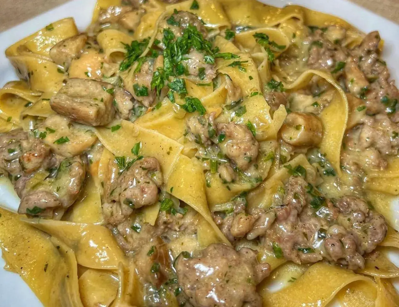 Pappardelle cremose con un saporito sugo di pasta salsiccia e funghi, guarnite con prezzemolo fresco.
