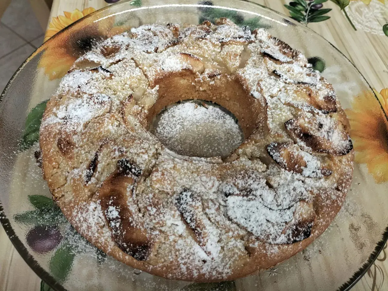 Torta all'acqua soffice e profumata, cosparsa di zucchero a velo, con pezzi di mela visibili.