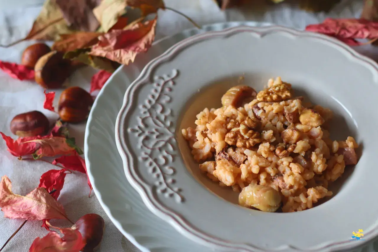 Un cremoso risotto castagne e gorgonzola, guarnito con noci e castagne intere, su un piatto decorato, circondato da foglie autunnali e castagne.