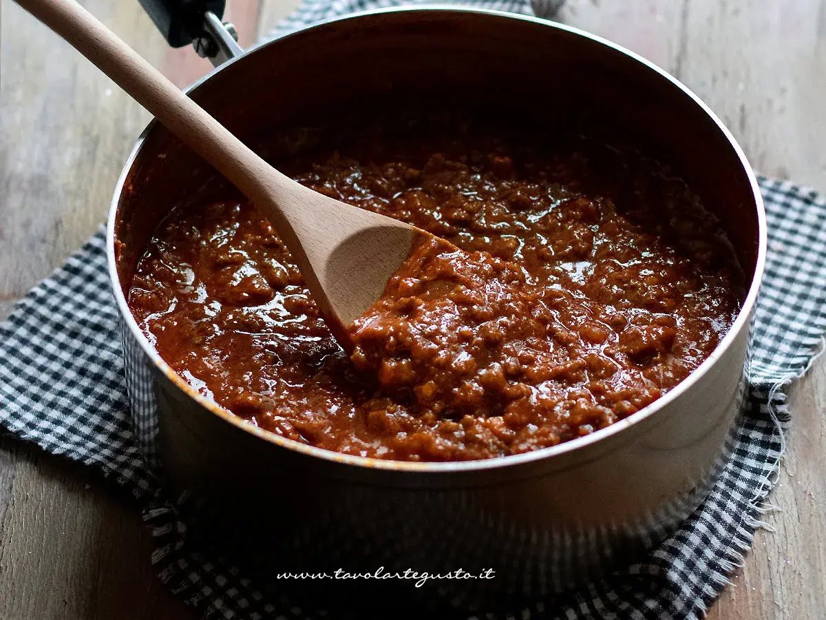 Un pentolino pieno di ragù alla bolognese, pronto per condire la pasta. Un cucchiaio di legno affonda nella salsa densa e profumata.