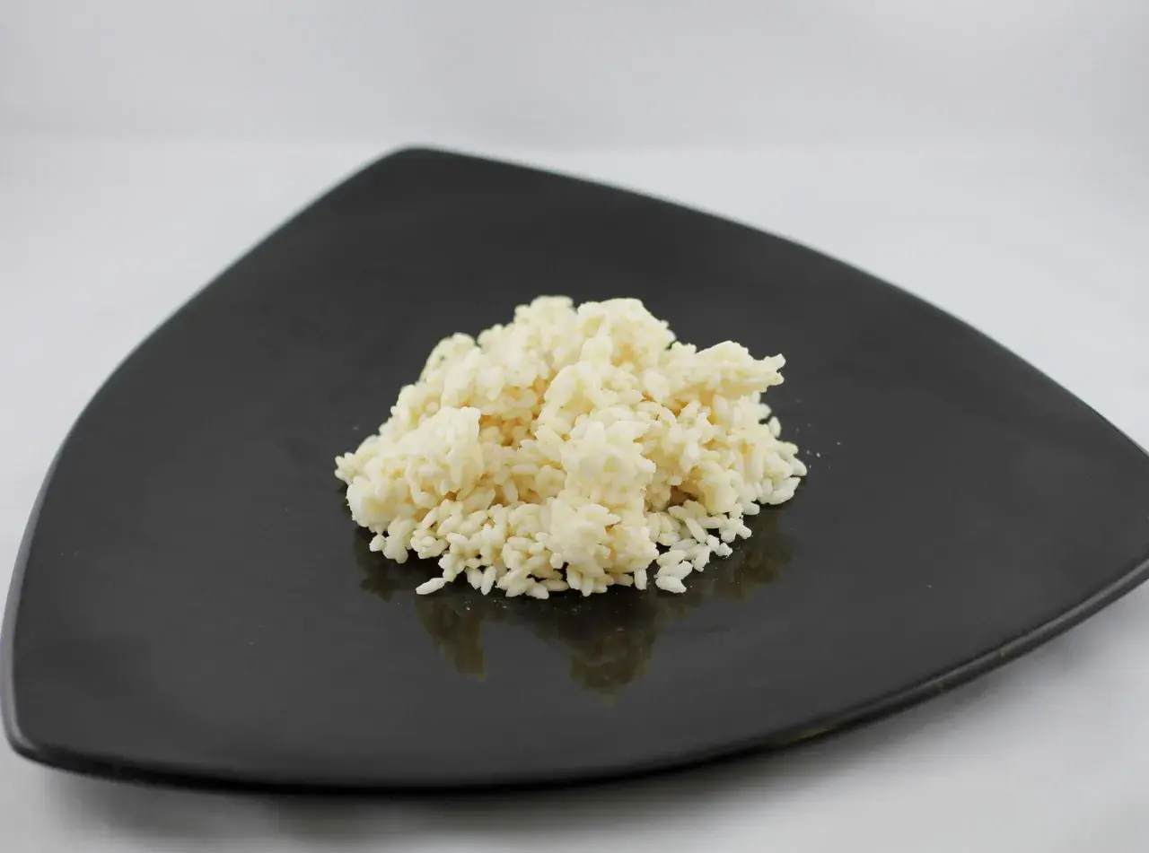 Un mucchietto di riso bianco cotto su un piatto nero, pronto per essere gustato. Ecco come cuocere il riso per un risultato perfetto.