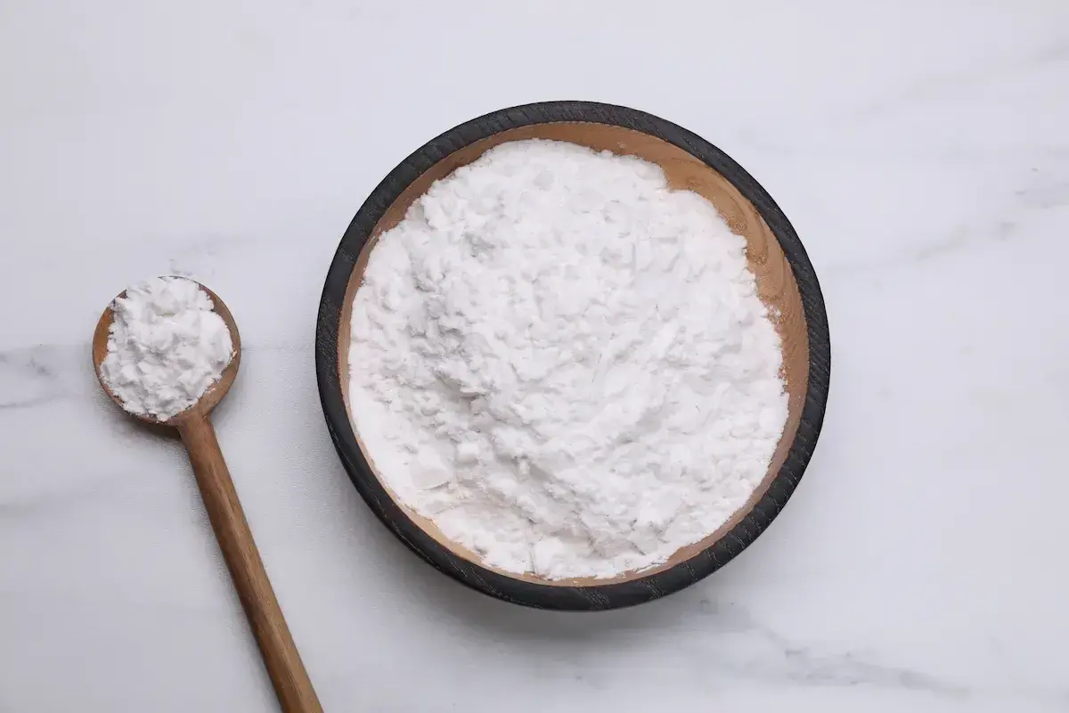 Una ciotola di amido di riso per dolci, con un cucchiaio di legno pieno dello stesso ingrediente soffice.