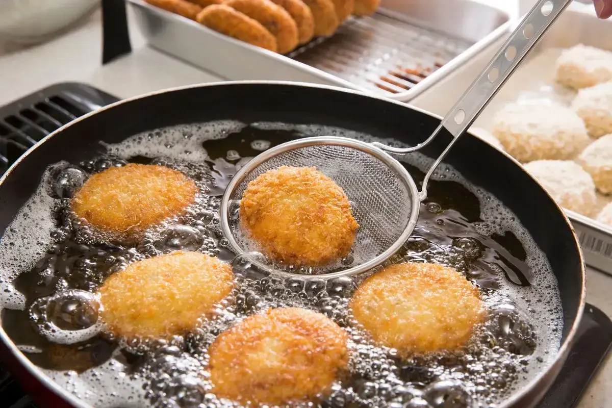 Crocchette dorate che sfrigolano nell'olio bollente, un perfetto esempio di come friggere per ottenere una croccantezza irresistibile.