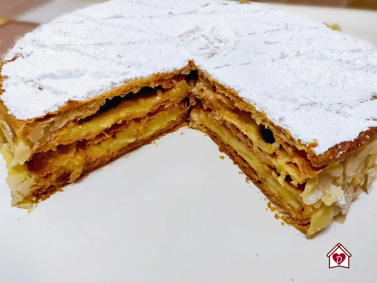 Una deliziosa torta millefoglie con strati di pasta sfoglia croccante e crema pasticcera, cosparsa di zucchero a velo e mandorle.
