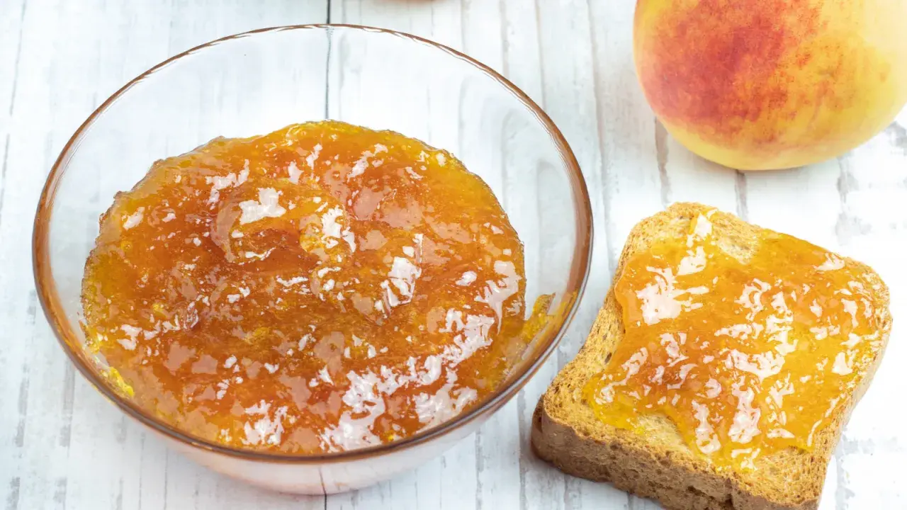 Una ciotola di marmellata di pesche fatta in casa e una fetta biscottata imburrata con la stessa deliziosa marmellata.