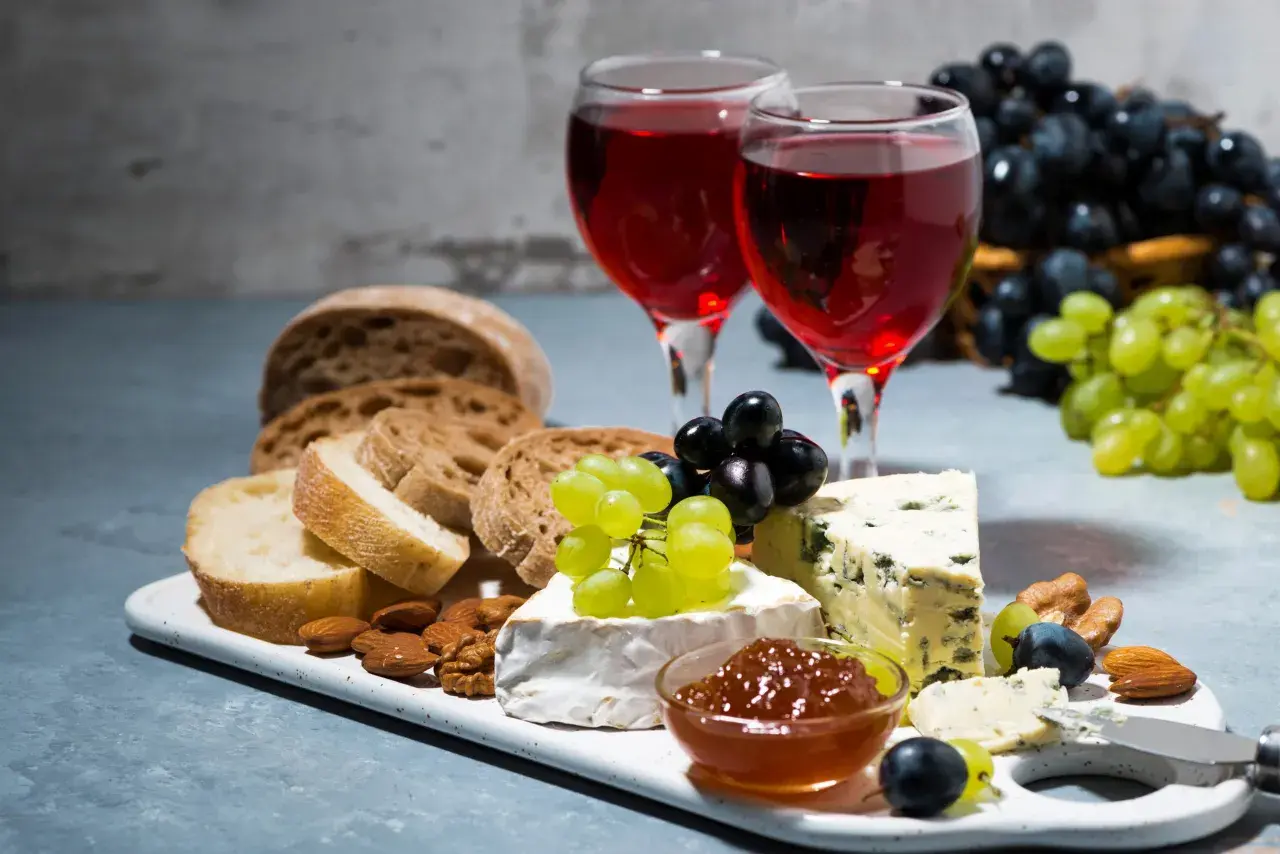 Due calici di rosato vino accompagnano un tagliere con pane, formaggi, uva e frutta secca.