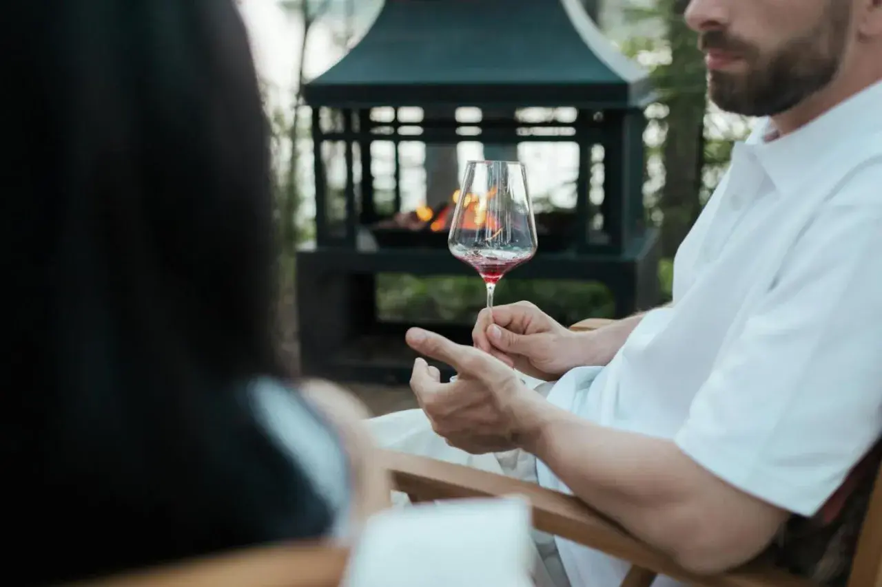 Uomo con barba tiene un calice di vino rosso, mostrando come si tiene il calice di vino per il gambo, vicino a un braciere acceso.