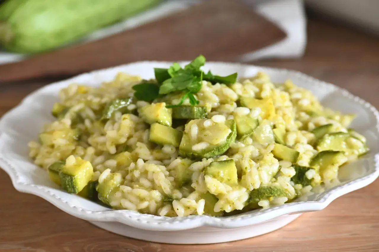Un cremoso risotto con zucchine, guarnito con prezzemolo fresco, servito in un piatto bianco.