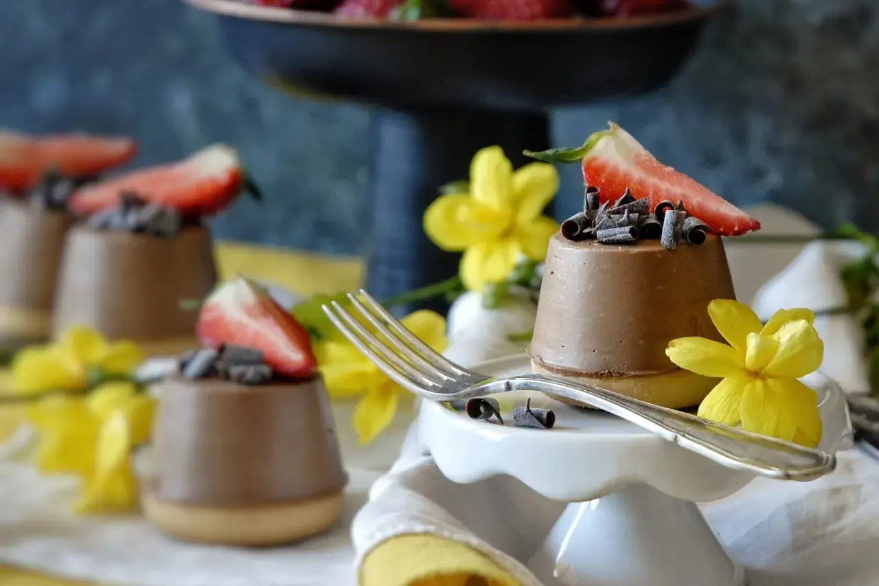 Mini cheesecake al cioccolato con fragola e riccioli di cioccolato, decorati con fiori gialli.