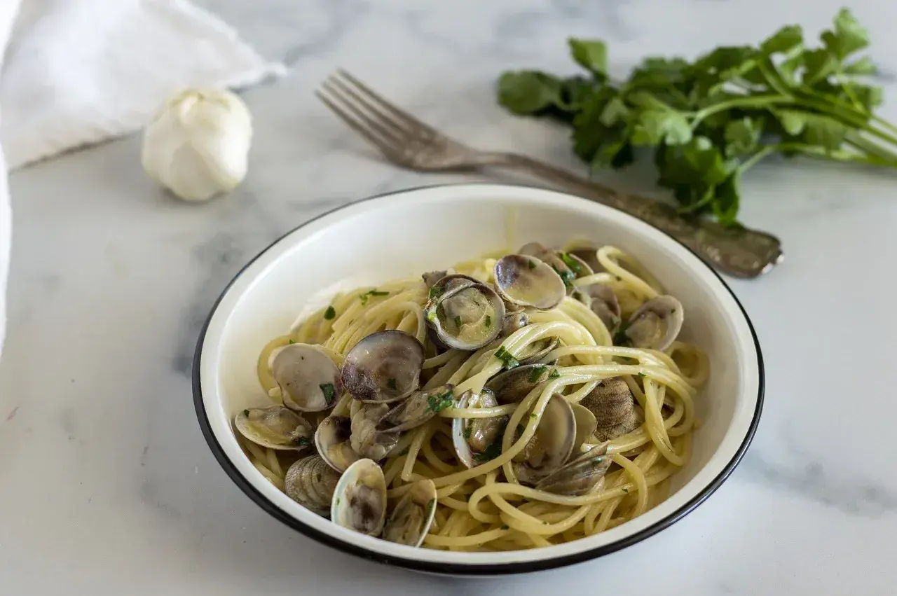 Un piatto invitante di spaghetti alle vongole, con aglio e prezzemolo freschi sullo sfondo.