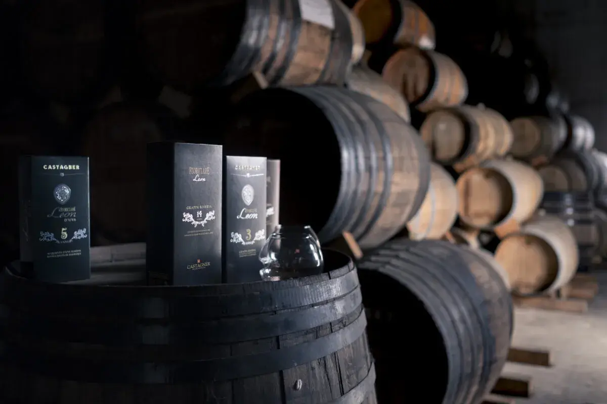 Bottiglie di grappa Castagner su botti di legno. Il significato di grappa barricata è legato all'affinamento in botte, che dona colore e aromi complessi.