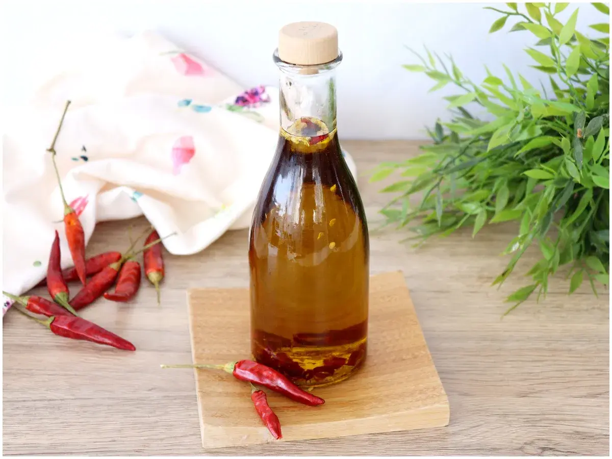 Una bottiglia di olio al peperoncino, con peperoncini rossi secchi sparsi intorno e un tocco di verde sullo sfondo.