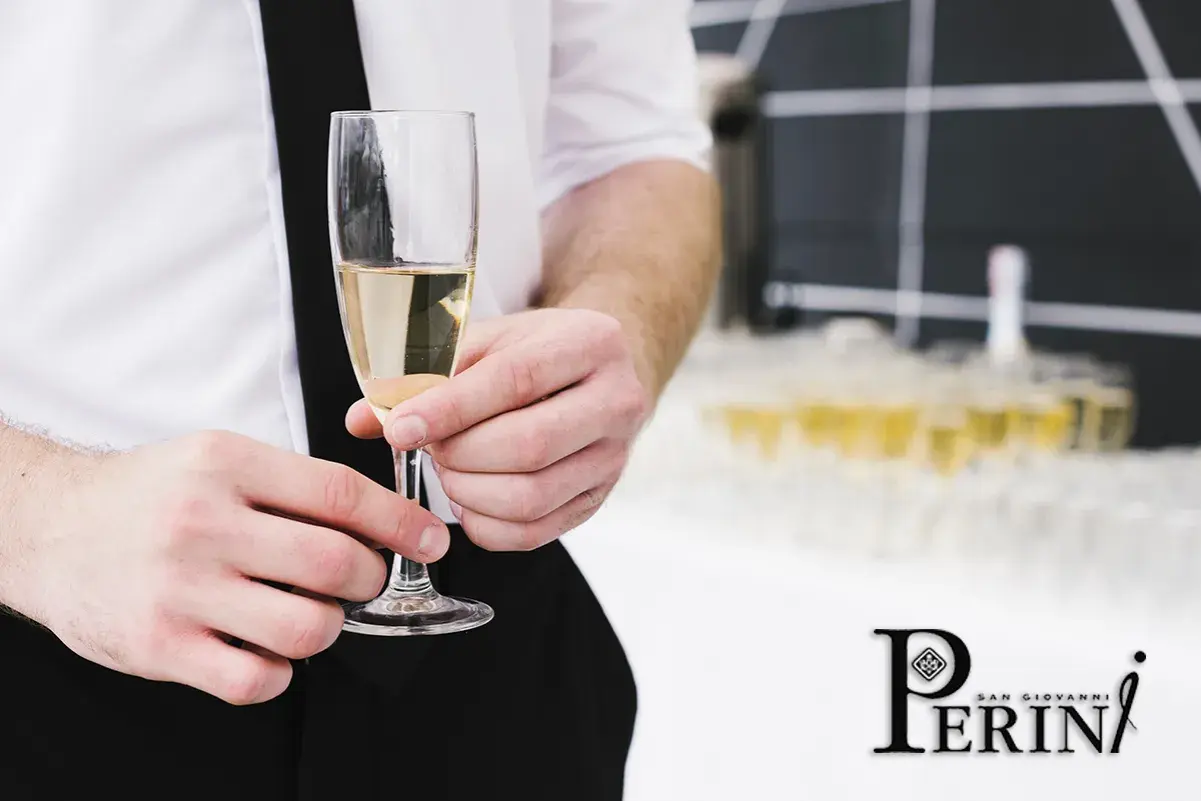 Un bicchiere di prosecco vino dorato, tenuto da mani eleganti, con una piramide di calici sullo sfondo.