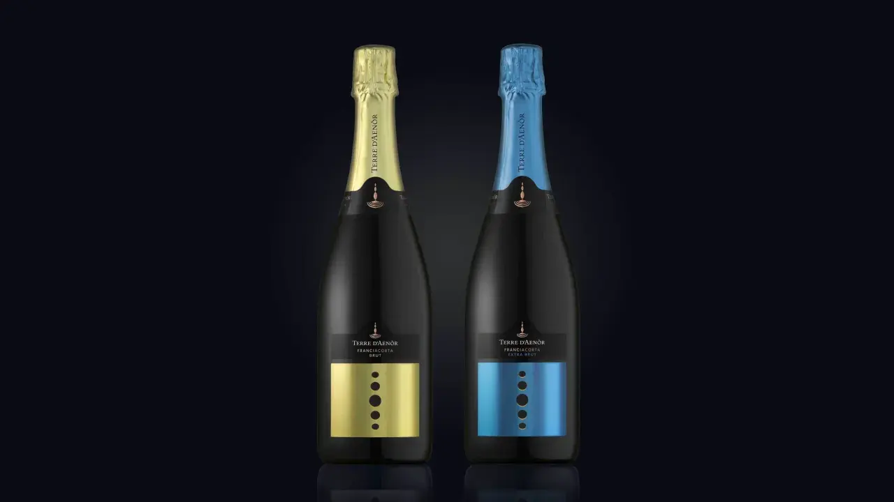 Due bottiglie di Franciacorta Terre d'Aenòr, una con capsula oro e etichetta oro, l'altra con capsula blu e etichetta blu. Entrambe sono Extra Brut, senza zucchero aggiunto.