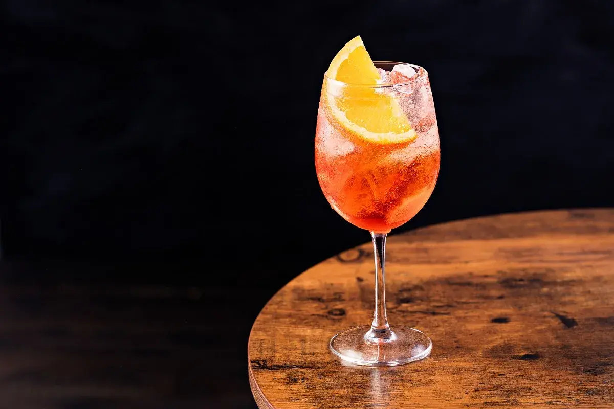 Un bicchiere di spritz Italia, rinfrescante e colorato, con una fetta d'arancia, su un tavolo di legno.