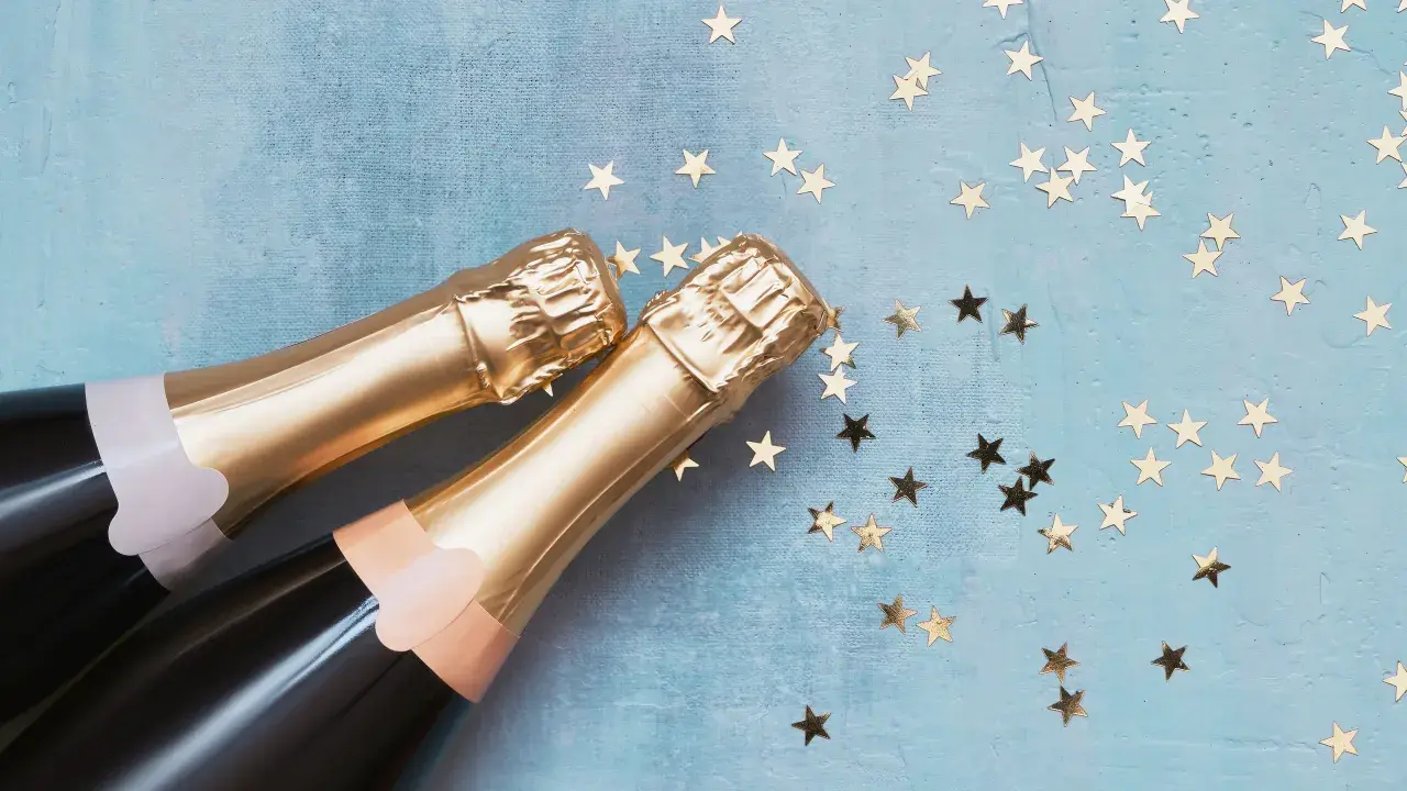 Due bottiglie di spumante dorato su sfondo blu con stelle dorate. Una celebrazione che fa pensare alla differenza tra prosecco e spumante.