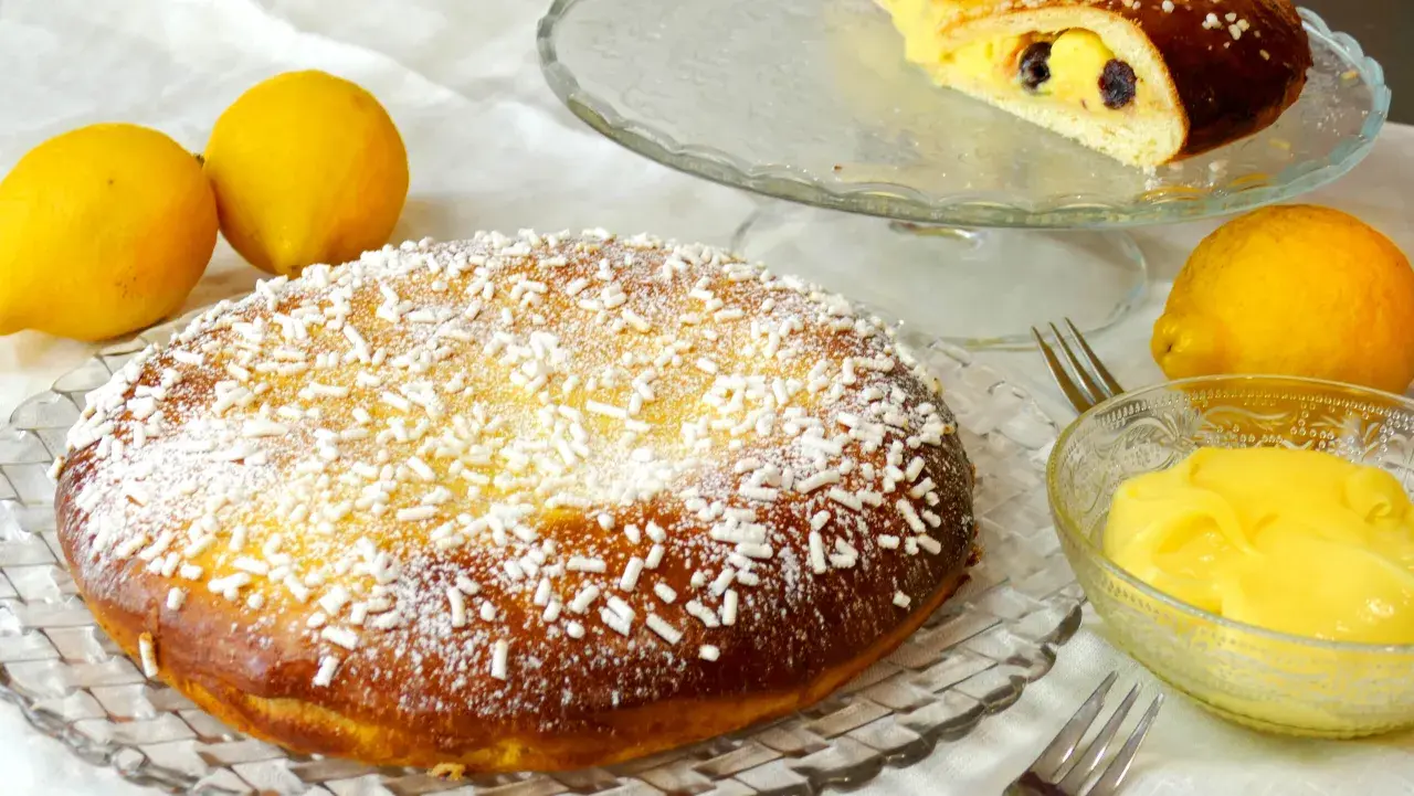 Una deliziosa polacca aversana, cosparsa di zucchero a velo e confettini, accanto a limoni freschi e crema pasticcera.