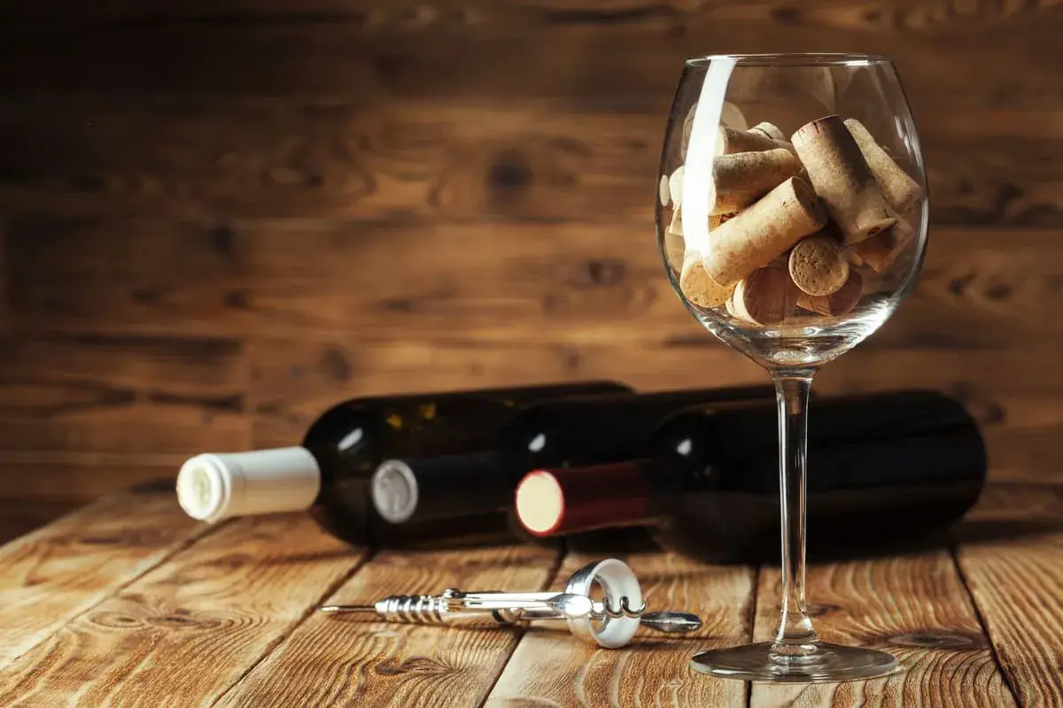 Tappi di sughero in un calice, bottiglie di vino e cavatappi sul tavolo. Un promemoria visivo su come chiudere una bottiglia di vino.
