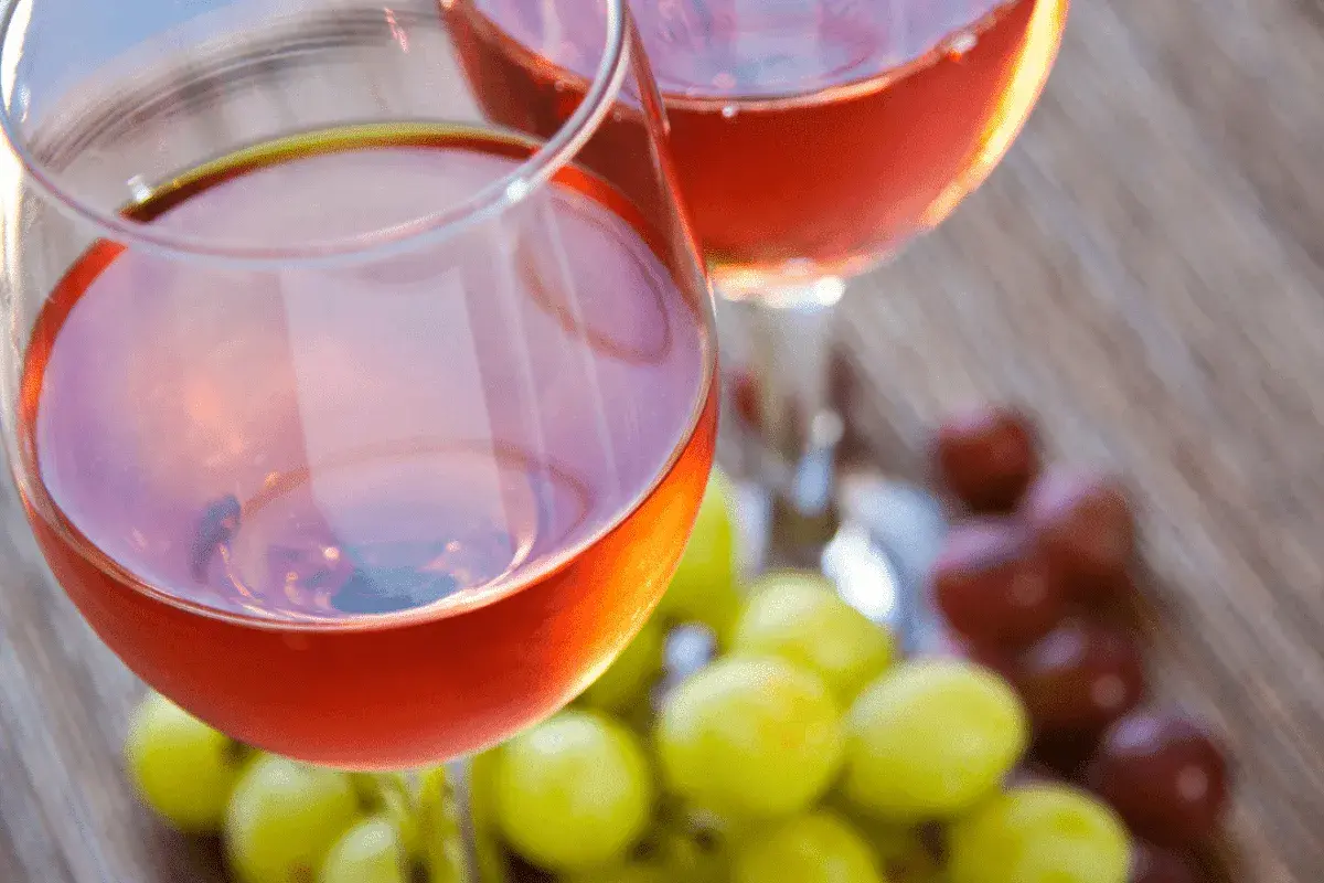 Due calici di vino rosato, frutto della vinificazione in rosato, con grappoli d'uva verde e rossa sullo sfondo.
