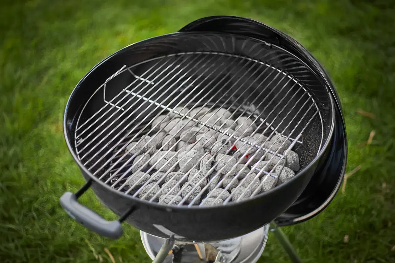 Carbone pronto per accendersi, quanta carbonella per una grigliata perfetta! La griglia è posizionata sopra, in attesa di cibo succulento.