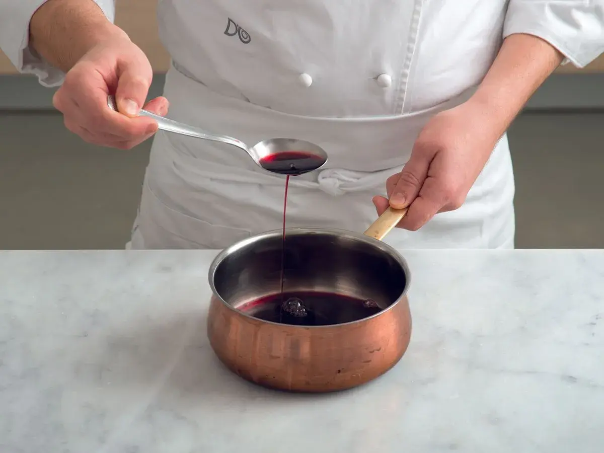 Chef versa un cucchiaio di riduzione di vino rosso in una pentola di rame.