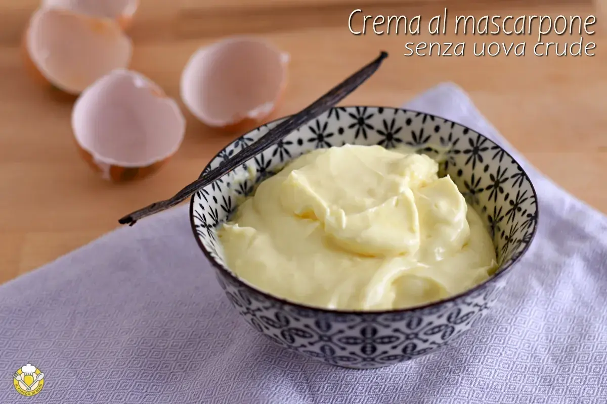Crema al mascarpone senza uova, soffice e vellutata, servita in una ciotola decorata con un baccello di vaniglia. Guscio d'uovo sullo sfondo.