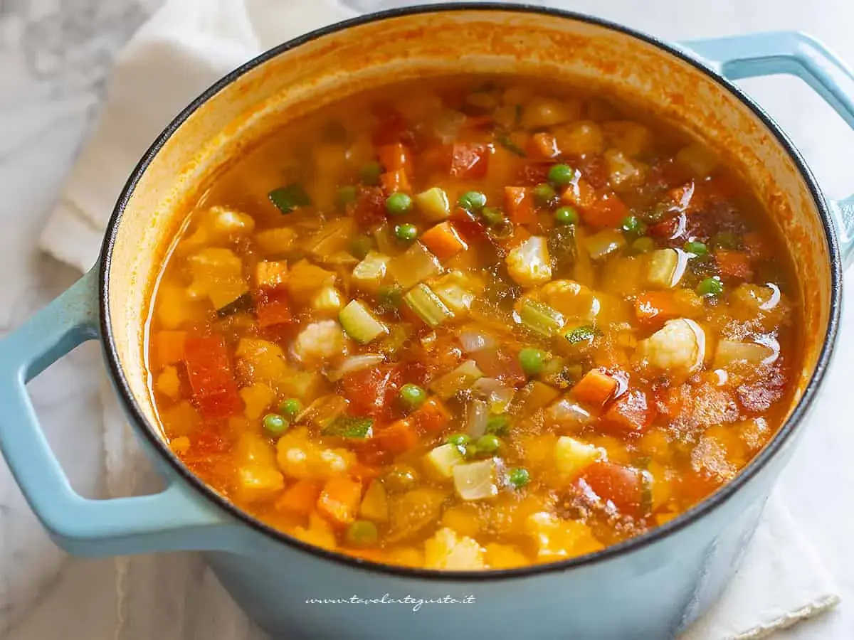 Un fumante minestrone di verdure in una pentola azzurra, ricco di carote, zucchine, piselli e cavolfiore.
