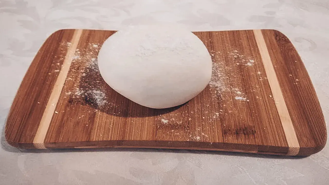 Palla di pasta di zucchero bianca su tagliere di legno, pronta per essere modellata.
