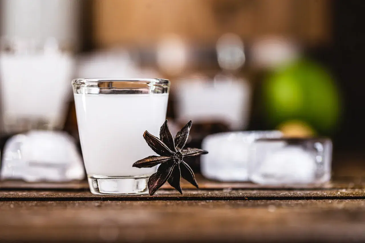 Un bicchierino di cocktail con la sambuca, guarnito con anice stellato, cubetti di ghiaccio e una fetta di lime sullo sfondo.