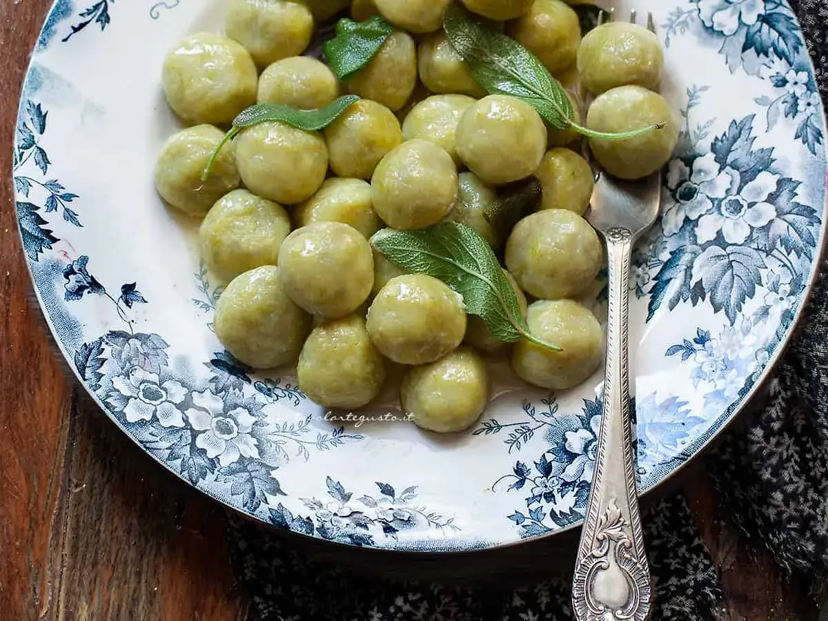 Gnocchi di zucchine soffici e profumati, guarniti con foglie di salvia fresca su un piatto decorato.
