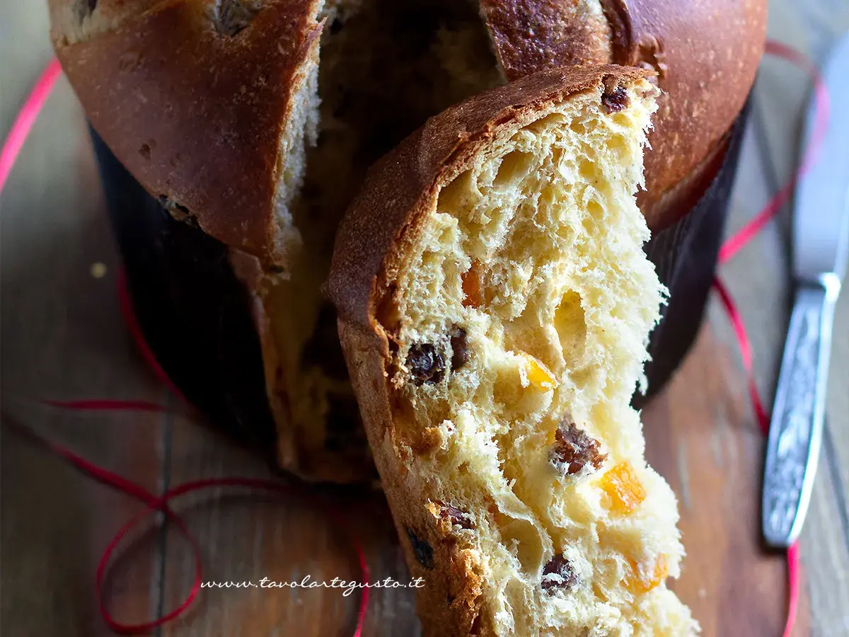 Un dolce panettone casalingo, soffice e profumato, con canditi e uvetta. Una fetta mostra la sua morbidezza e il colore dorato.