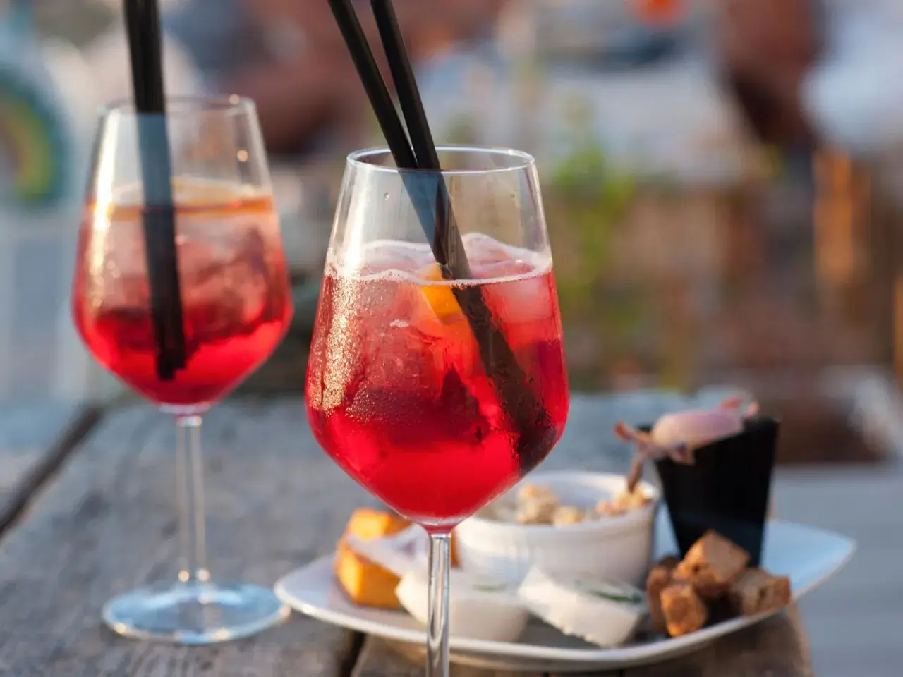 Due cocktail rossi con ghiaccio e arancia, accompagnati da stuzzichini. Perfetti per un aperitivo, ecco la pirlo bianco ricetta.