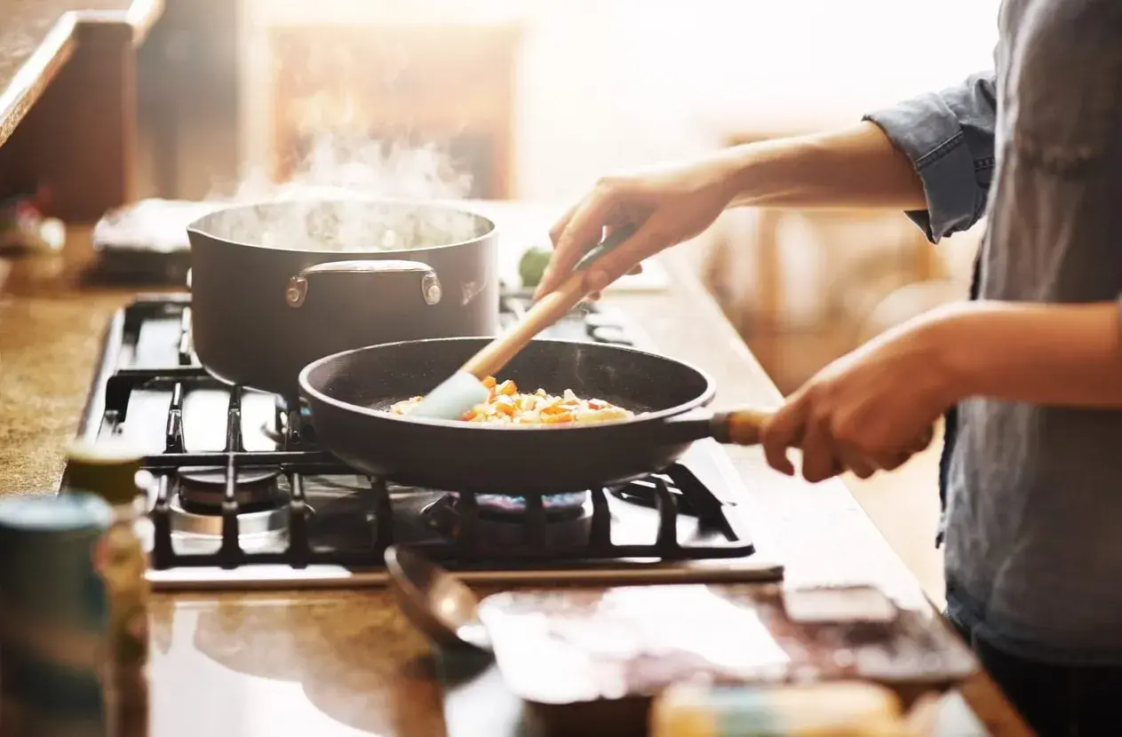 Mani che mescolano verdure in padella, mentre l'acqua bolle in pentola. Un'immagine che evoca il **macerare significato** in cucina: preparare ingredienti con cura.